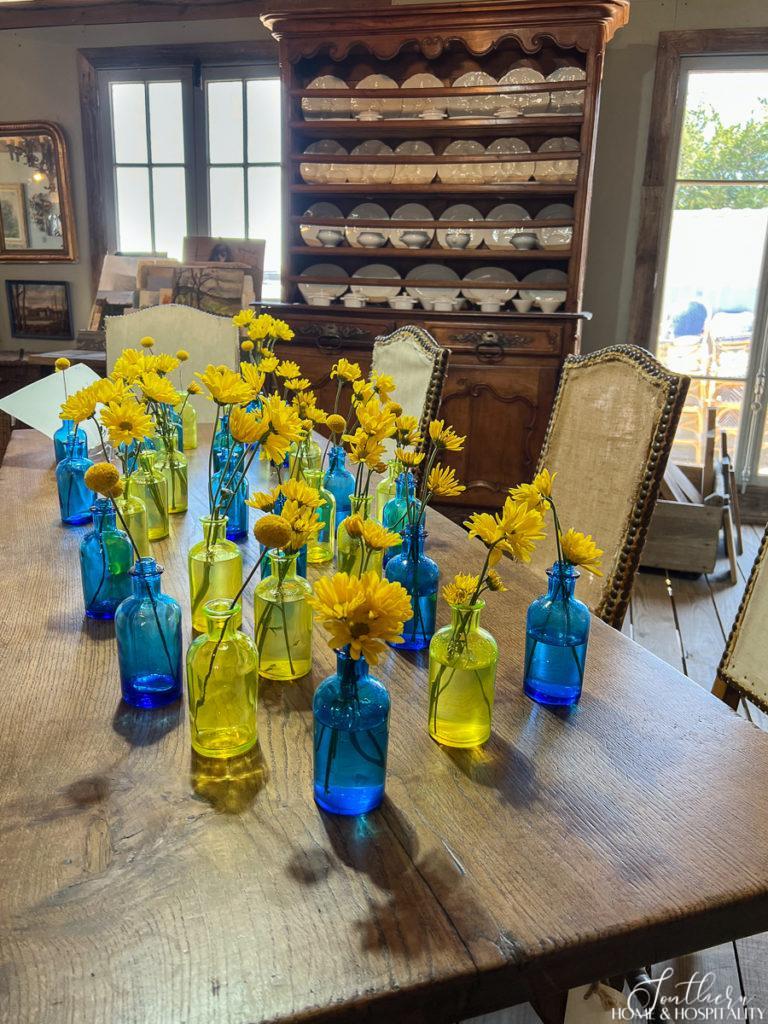 Collection of blue and yellow vases holding yellow daisies on a dining table