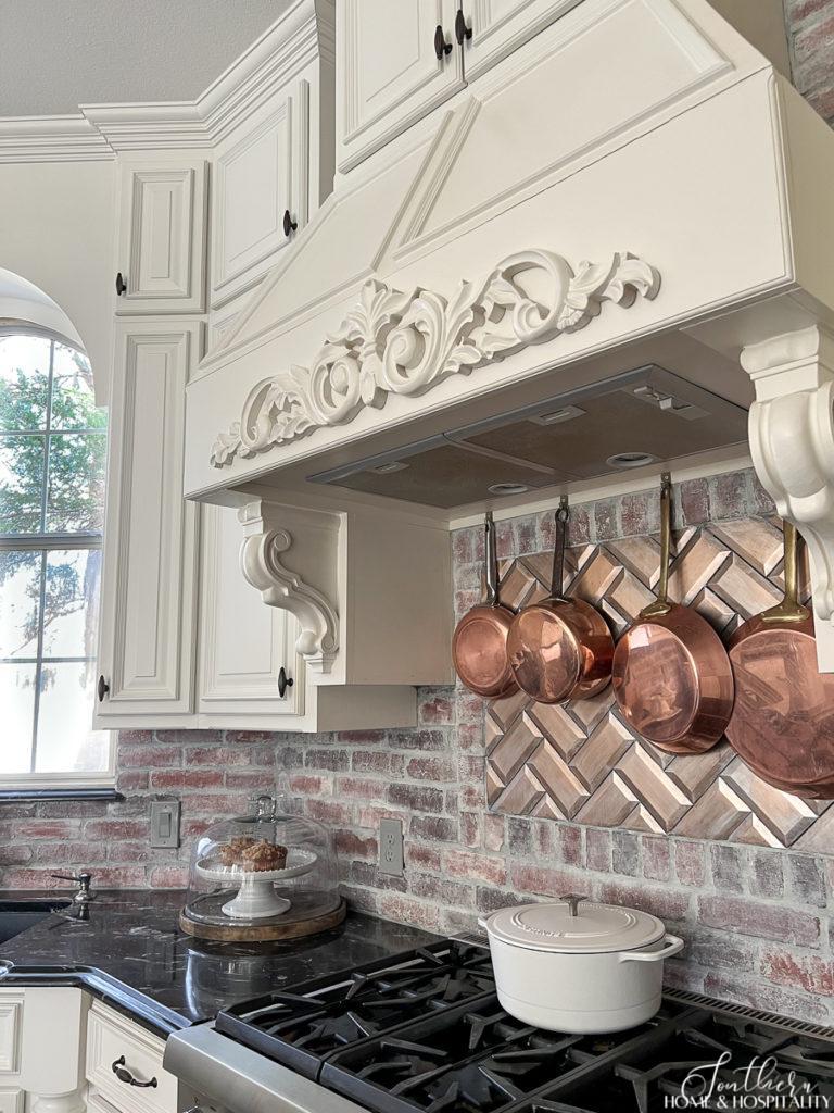 Copper pots hanging above cooktop in front of brick backsplash