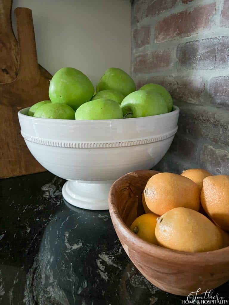 Green apples in white bowl and lemons in wood bowl on kitchen counter