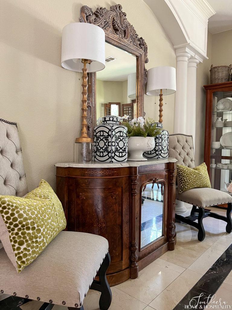 Mixing decorating styles with vintage sideboard, traditional French mirror, and modern lamps and throw pillows