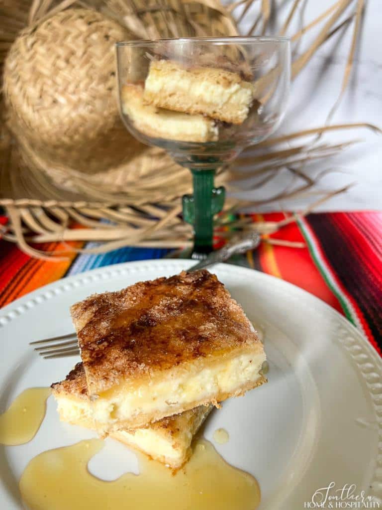 sopapilla cheesecake bars served on a white plate with honey and in a margarita glass