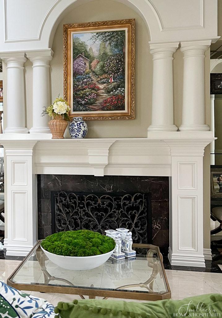 Southern traditional fireplace with columns and arch, marble surround, and colorful painting in ornate gold frame