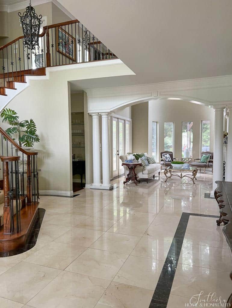 Traditional southern home living area and foyer with white marble floor with black accents, columns and arches