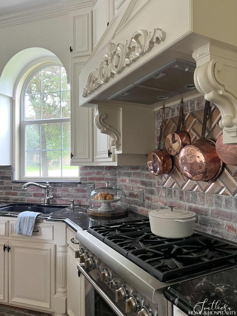 Copper pots hanging over stove, French country vent hood, brick backsplash