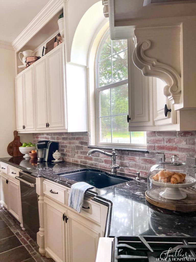 Traditional kitchen with brick backsplash, black counters, and white cabinets