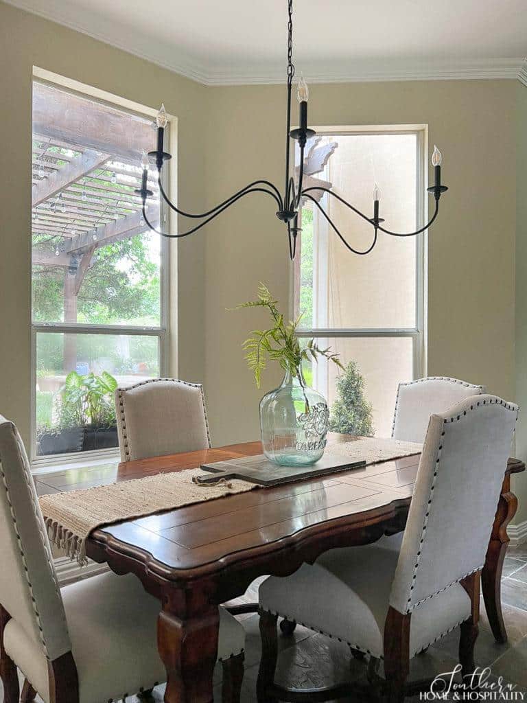 French country kitchen breakfast nook with iron chandelier, fern in glass wine jug vase