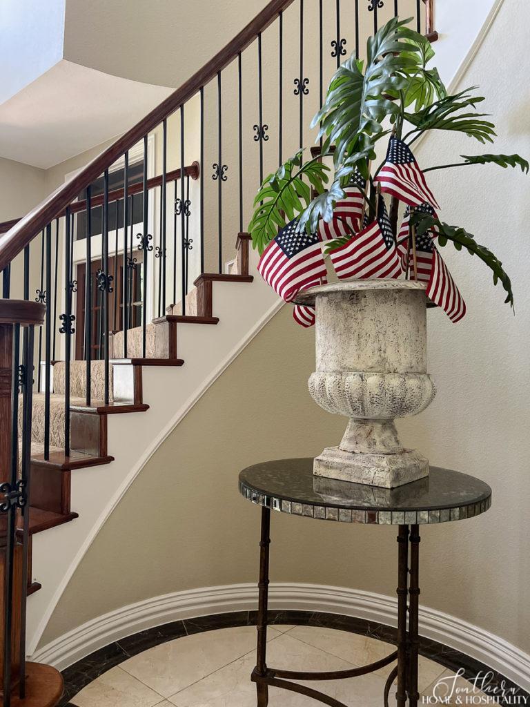 Large urn on mirrored foyer table with tropical plant and American flags