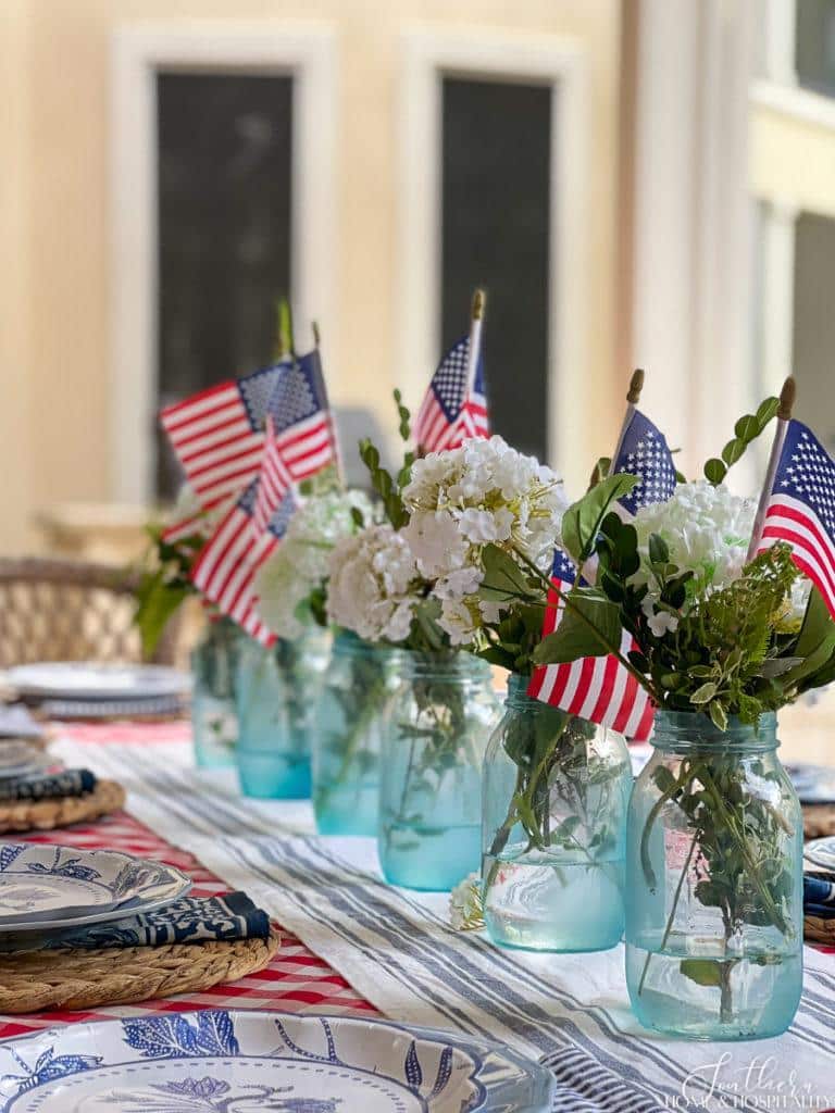 4th of July centerpiece with blue mason jars, white flowers, and flags