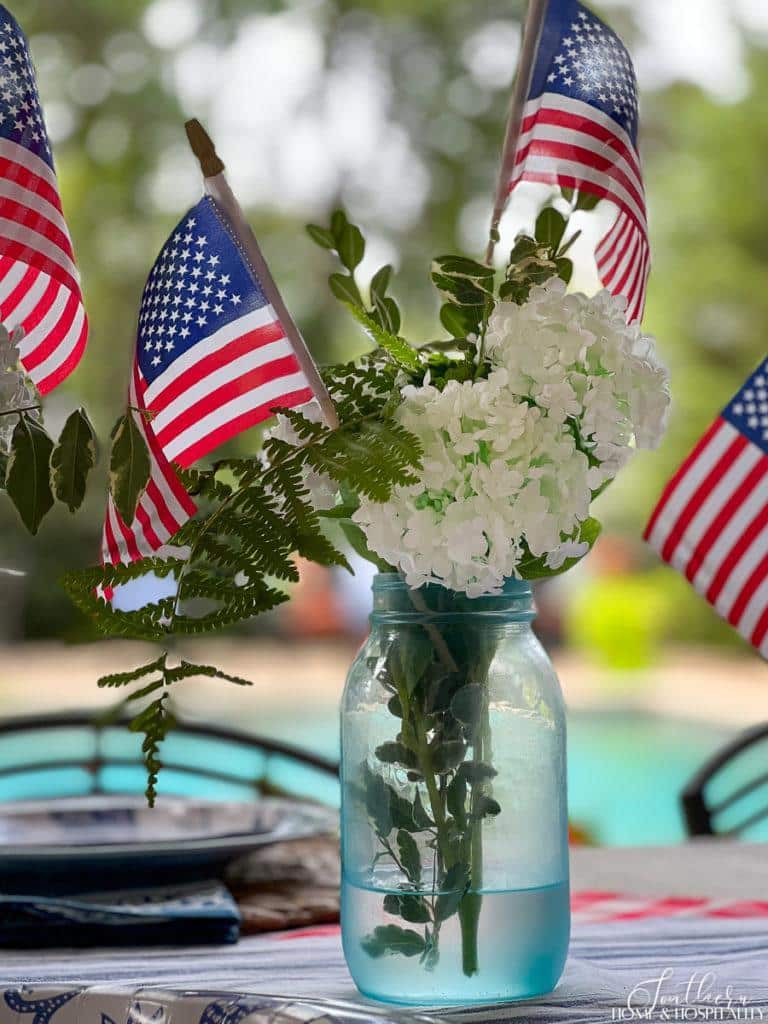 4th of July floral arrangement with white flowers, greenery, and flags in a blue mason jar