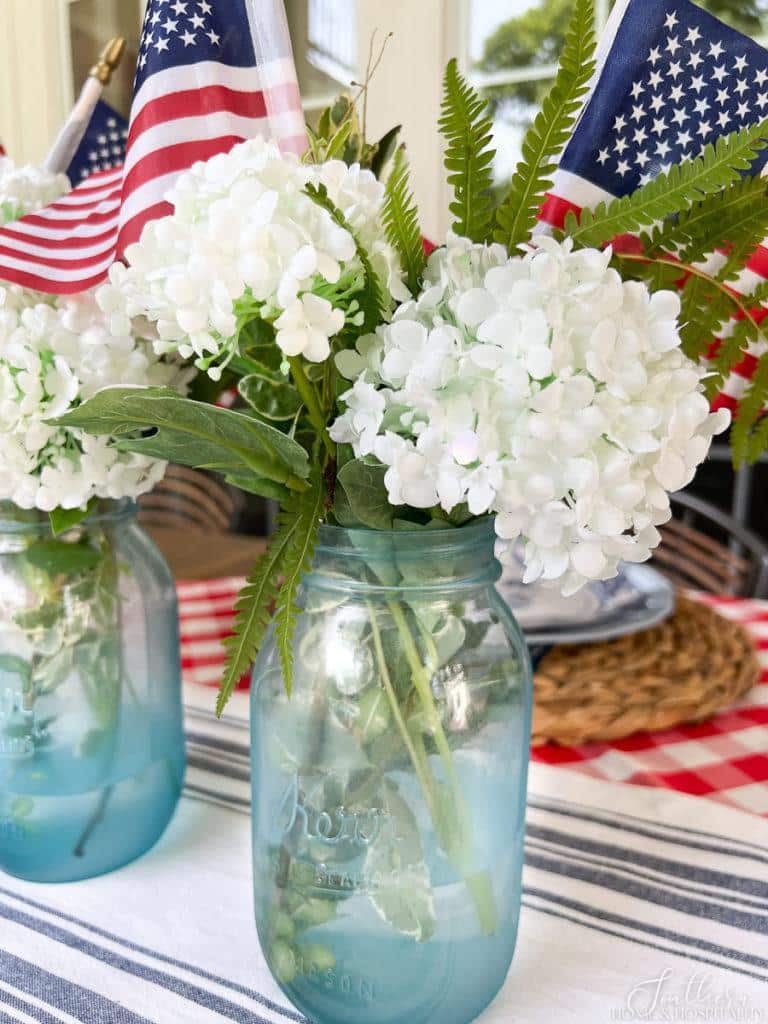 Mason jar painted with blue sea glass paint in a Fourth of July centerpiece with flags and white flowers