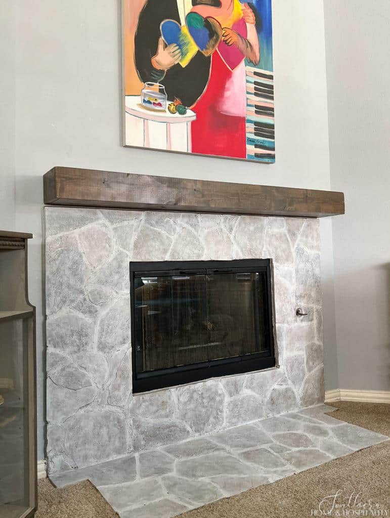 Whitewashed stone fireplace with stained wood mantel
