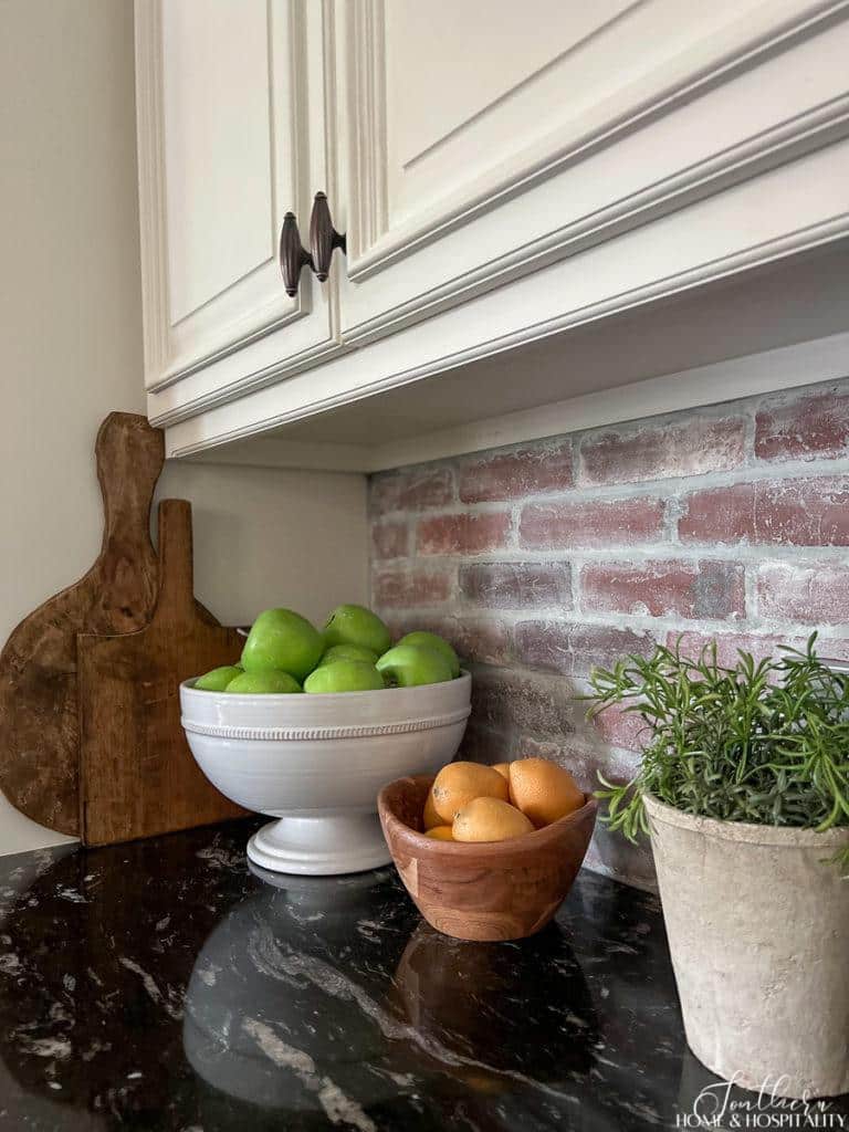 lemons in wood bowl, green apples in white bowl, rosemary in garden pot, brick backsplash