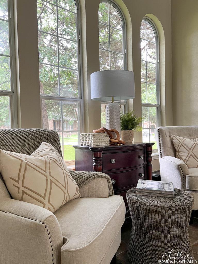 white fabric accent chairs, wicker ottoman, neutral throw pillows and green throw