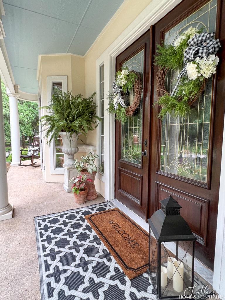 southern front porch with layered welcome mat, summer wreaths, large fern