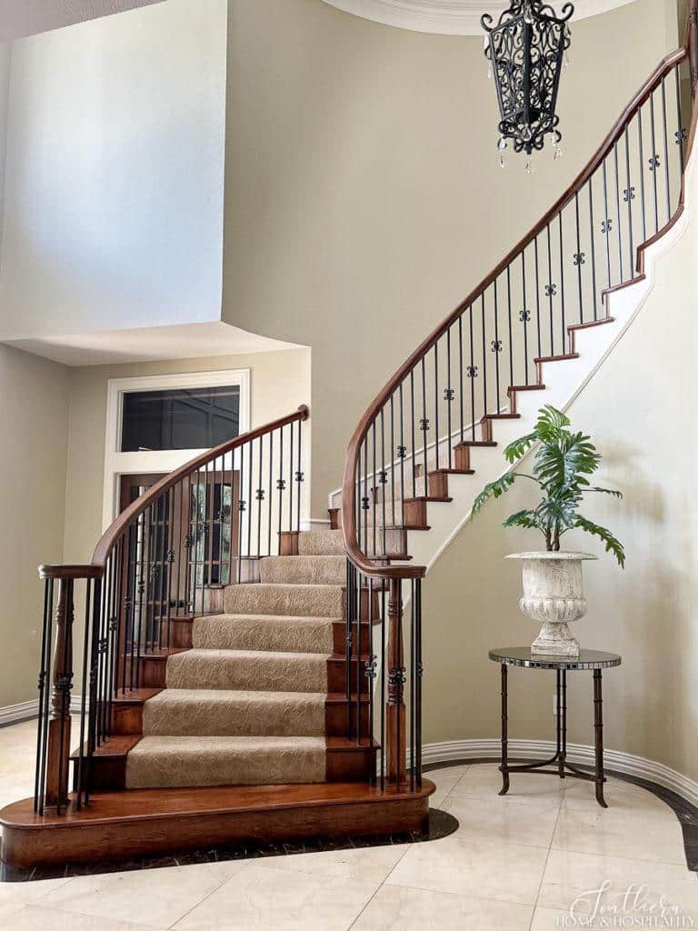 curved staircase with stained wood, iron balusters, and neutral sculptured carpet