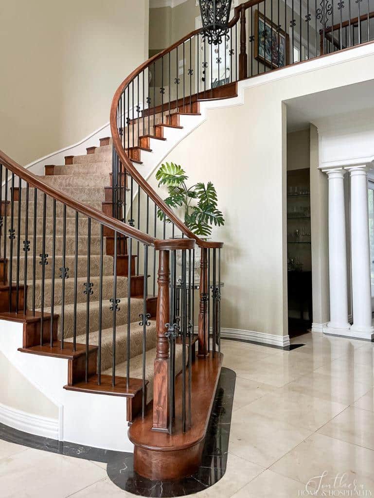 curved staircase with stained wood, iron balusters, and neutral sculptured carpet