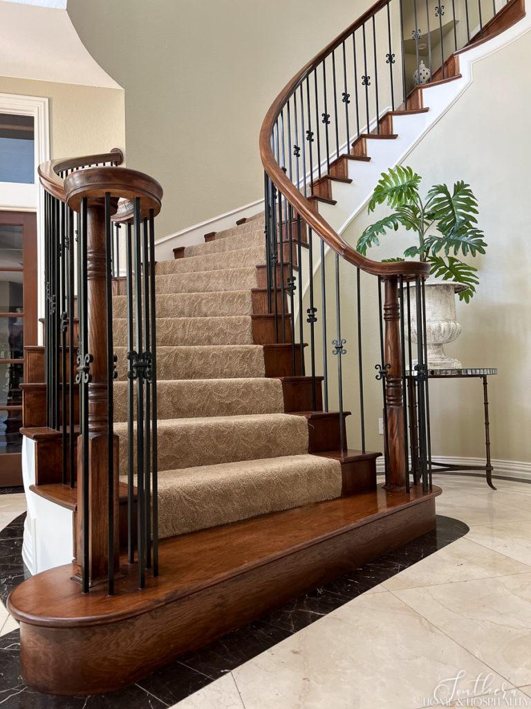 curved staircase with stained wood, iron balusters, and neutral sculptured carpet