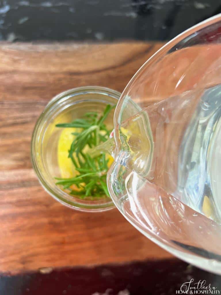 pouring water into an insect repellant candle mason jar with rosemary and lemon