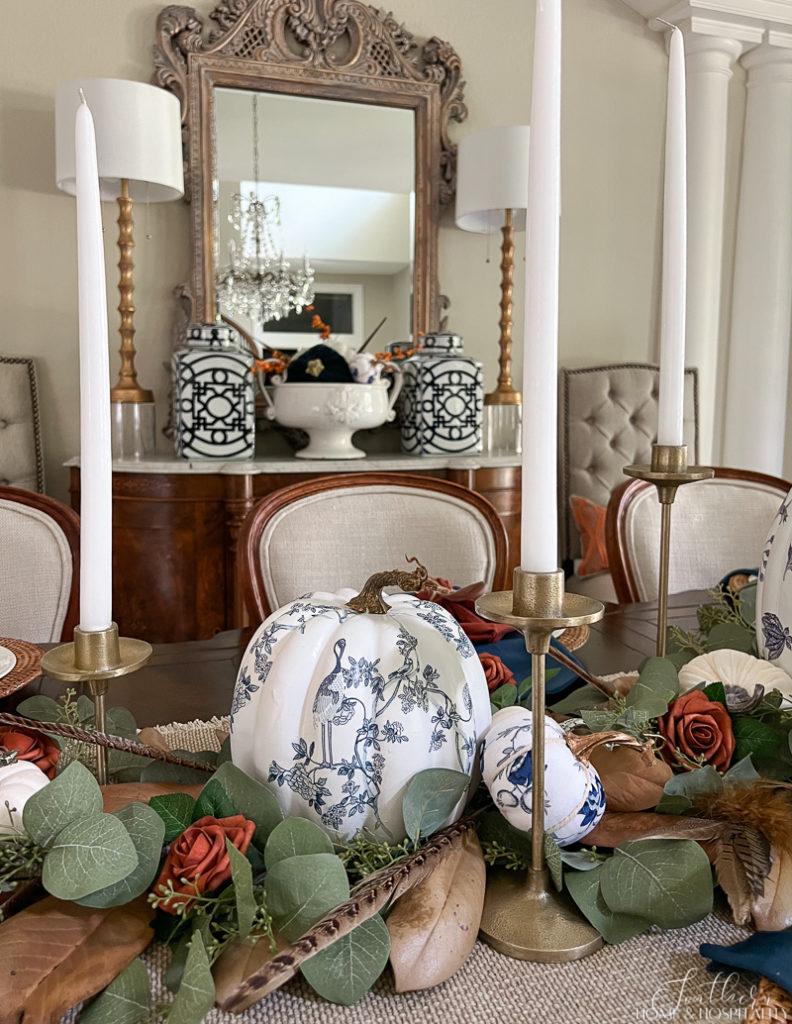 Chinoiserie pumpkins, magnolia leaves, and pheasant feathers in dining table centerpiece