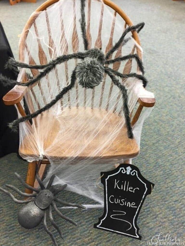 Halloween spider webs stretched over chair with furry spider and chalkboard tombstone