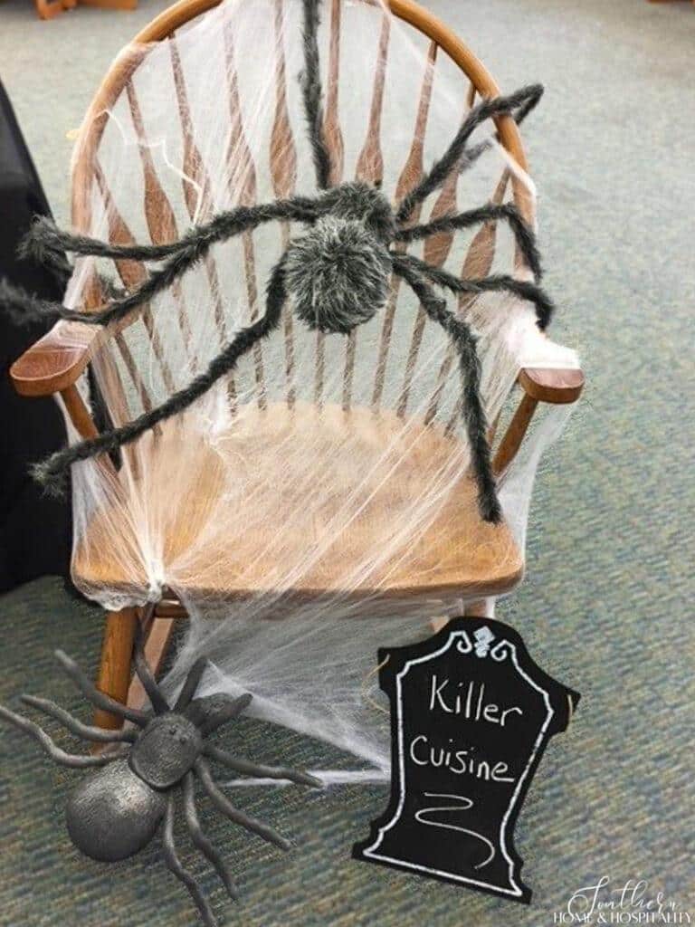 Halloween spider webs stretched over chair with furry spider and chalkboard tombstone