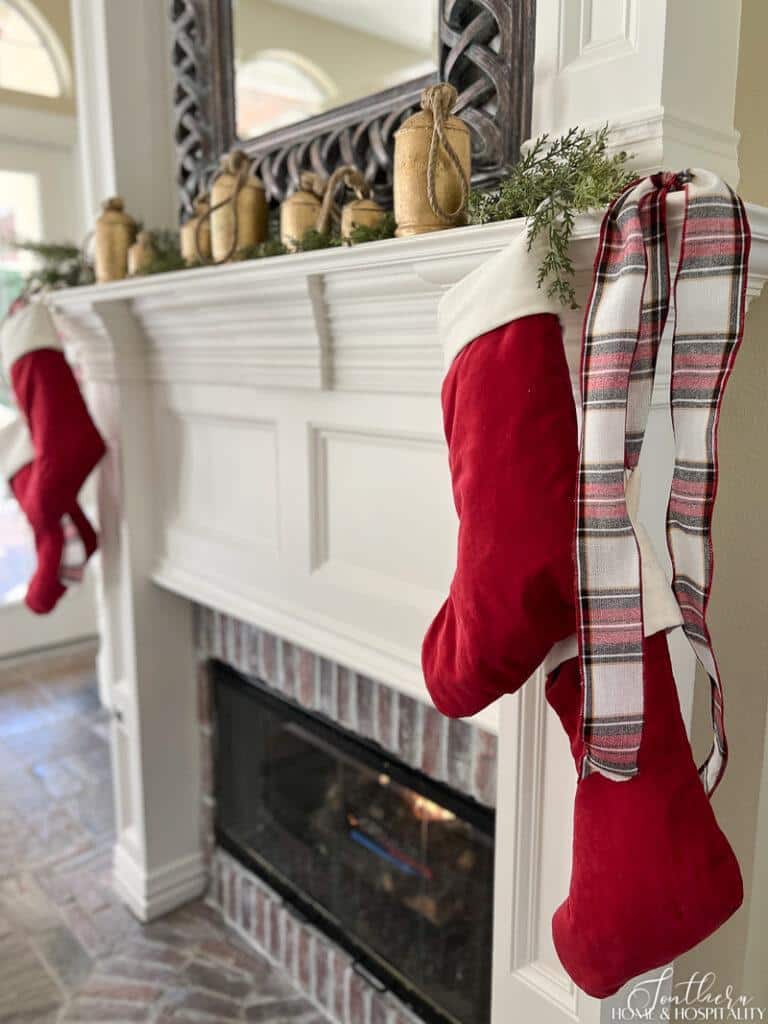 Fireplace with rustic Christmas bells and red velvet stockings with plaid ribbon on mantel