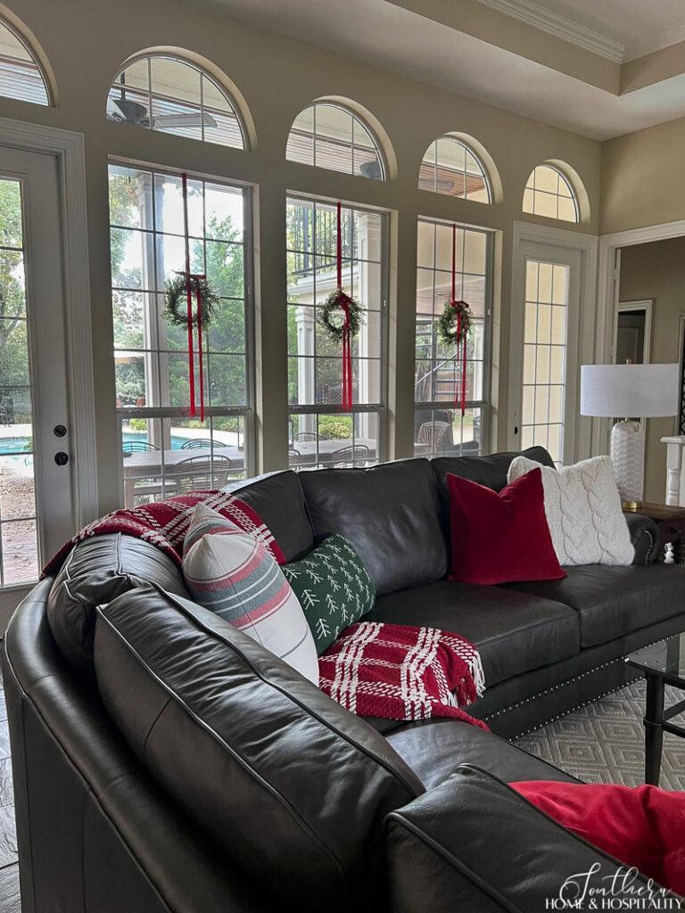 Christmas pillows on leather sectional, wreaths on family room windows