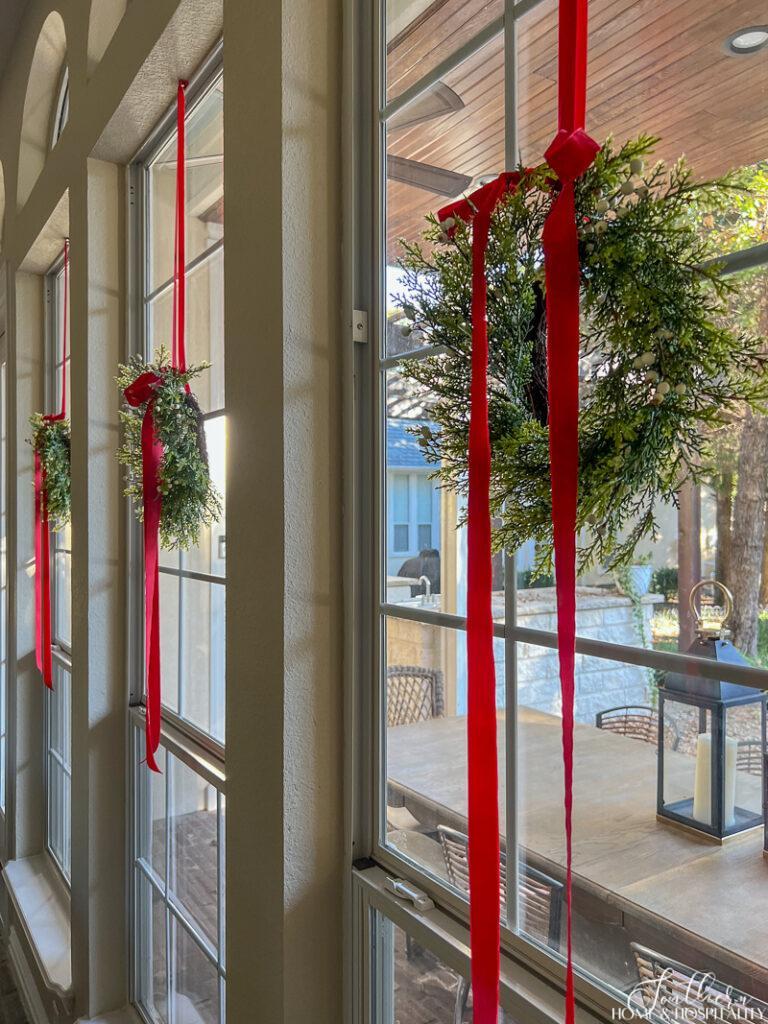 Christmas wreaths hung on inside windows with ribbon