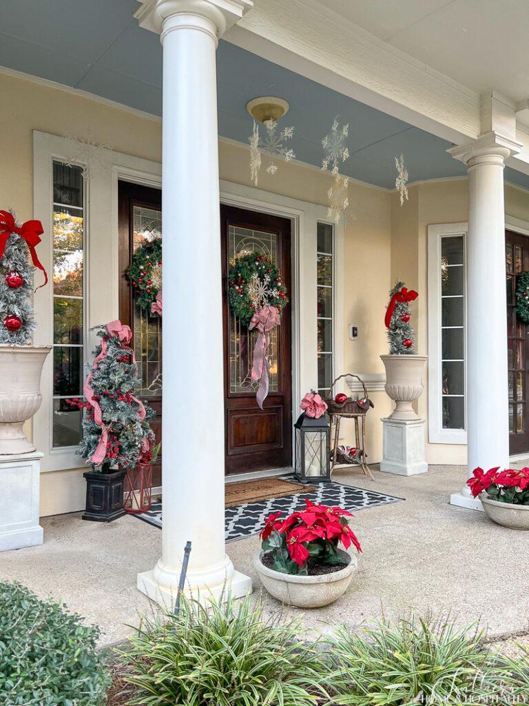 Porch decorated for Christmas with holiday topiaries in planters and poinsettias