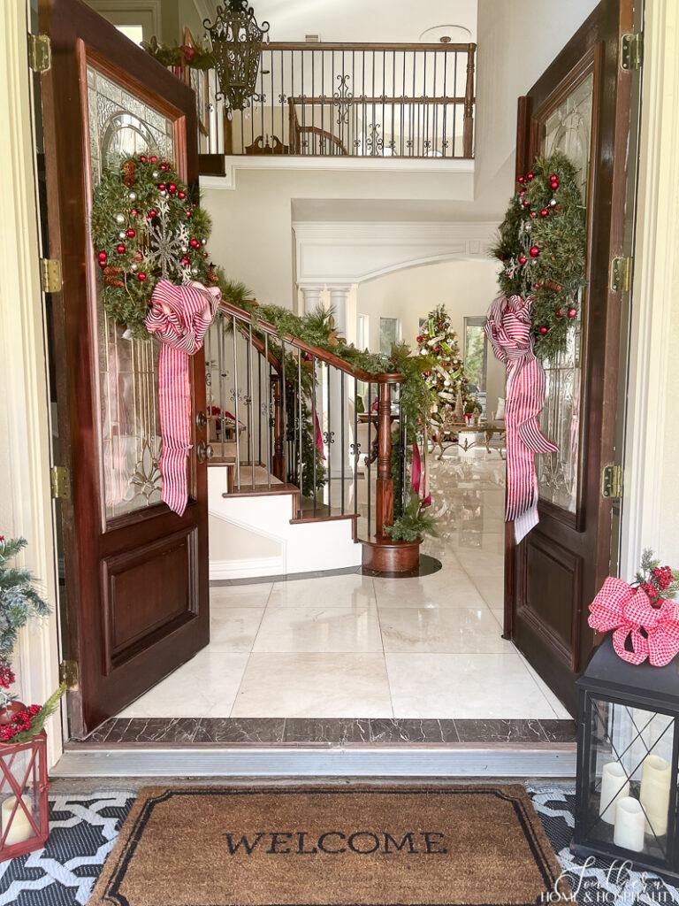 Double front doors with Christmas wreaths open to staircase decorated with garland