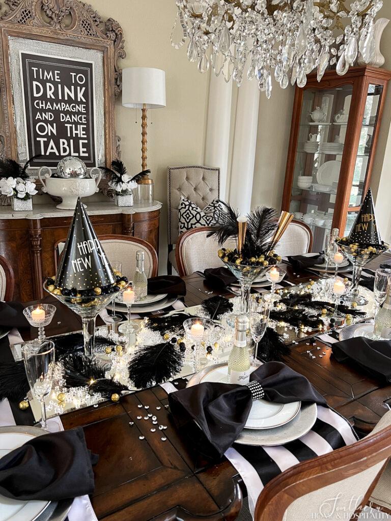 Long New Year's Eve dining table decorated with silver and gold accents, glass centerpieces, candles, and elegant place settings