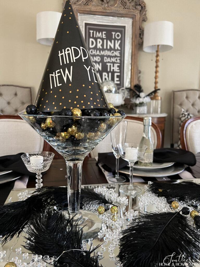 Large martini glass with black and gold balls and Happy New Year party hat