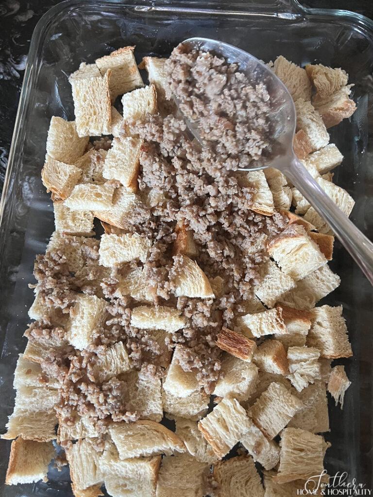 Spooning crumbled sausage over bread cubes