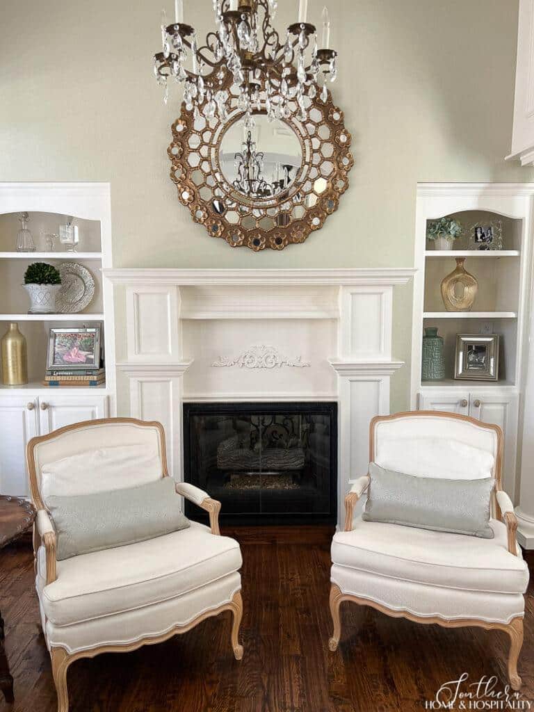 Master bedroom sitting area with fireplace and builtins and green walls, French chairs and starburst mirror