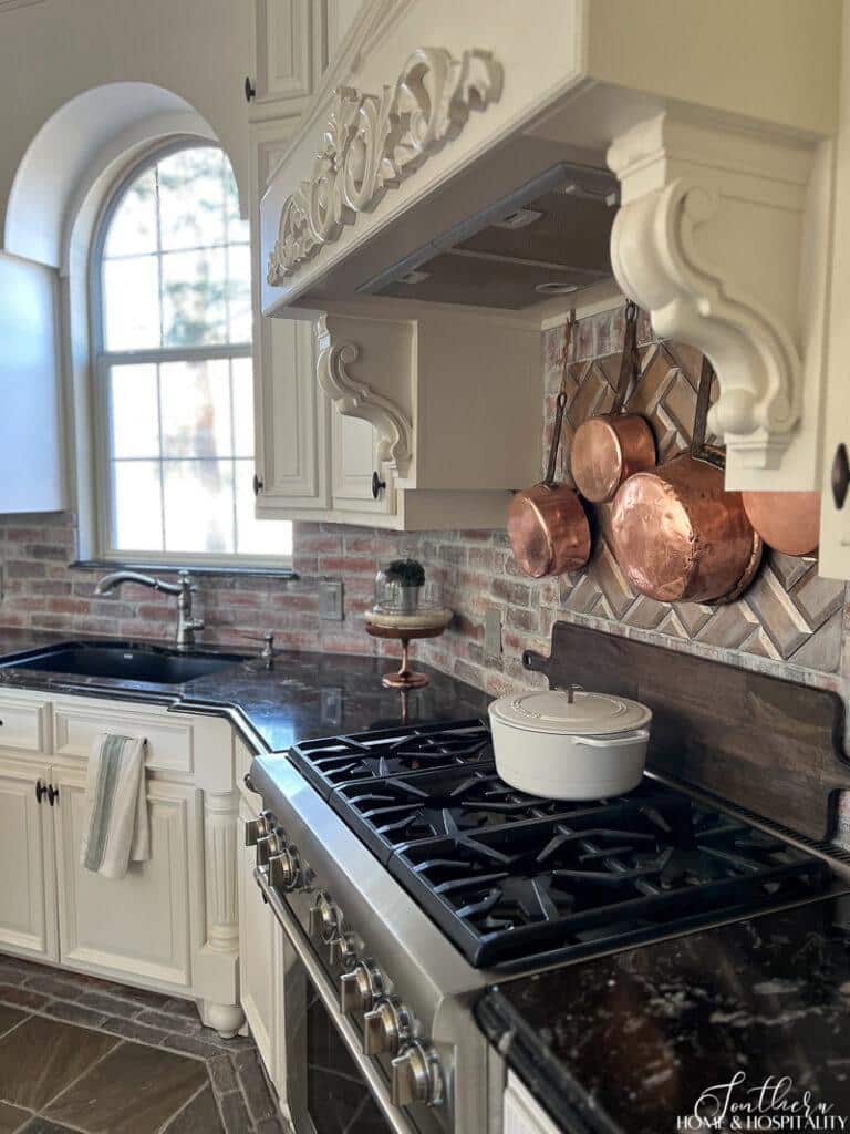 French country kitchen with copper pots, black counters, and white cabinets