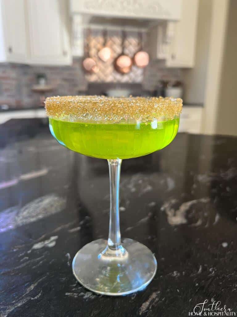 Green champagne cocktail with gold sugar in a coupe glass