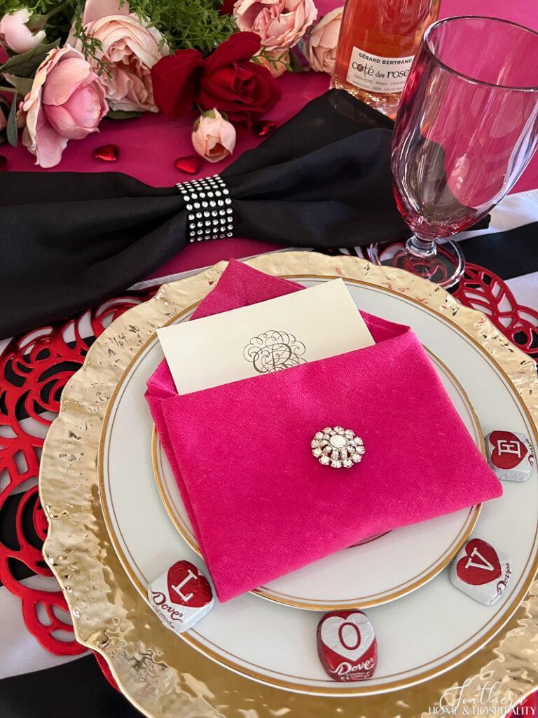 Envelope napkin fold with hot pink napkin, rhinestone brooch, and valentine card