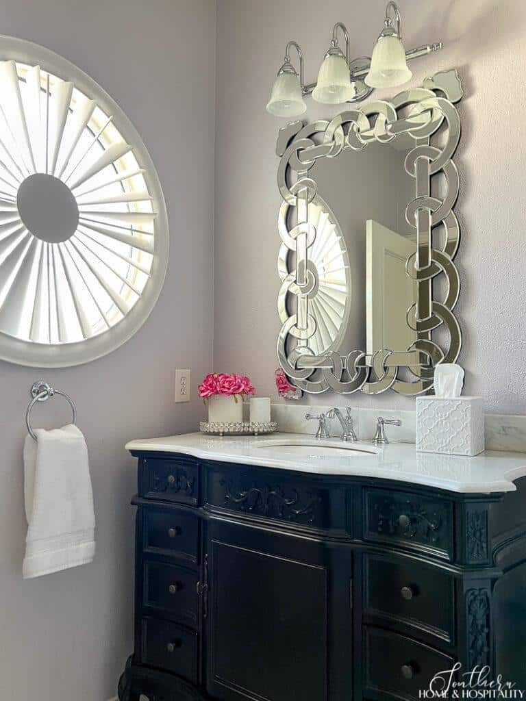 Black bathroom vanity with white marble top, venetian mirror, and lavender wall paint