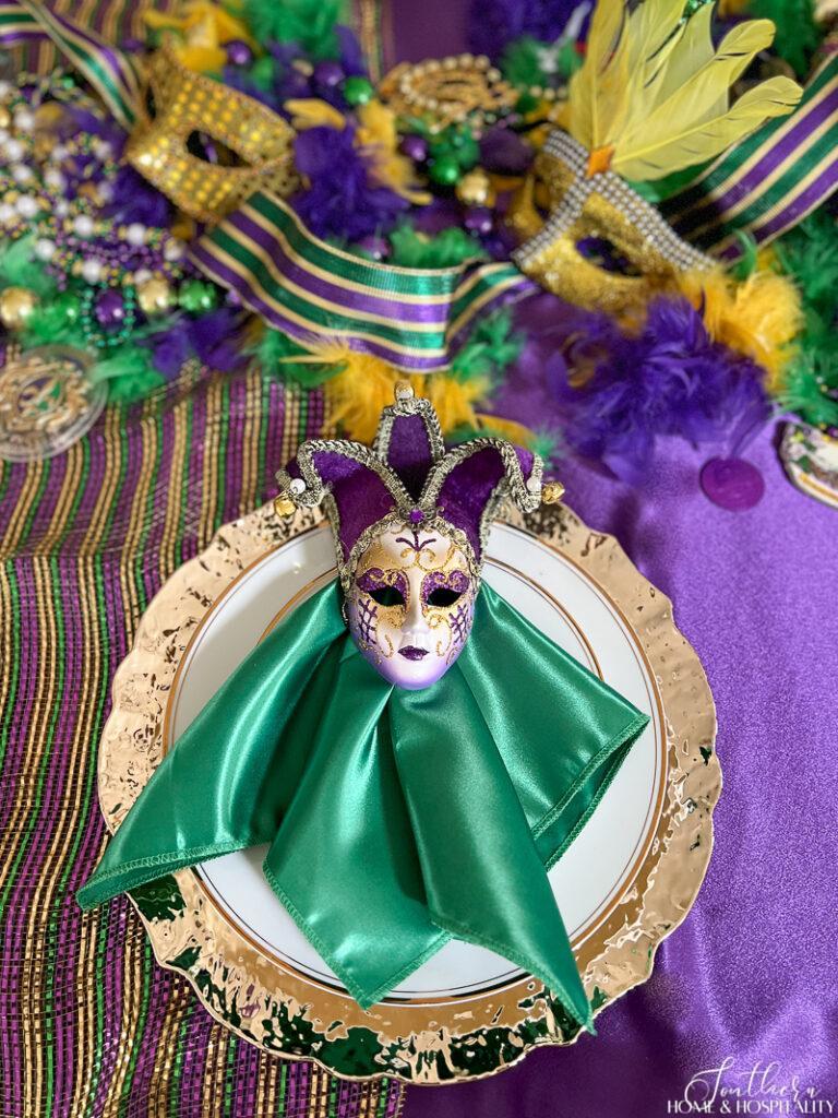 Mardi Gras place setting with jester mask, satin green napkin, gol charger plate