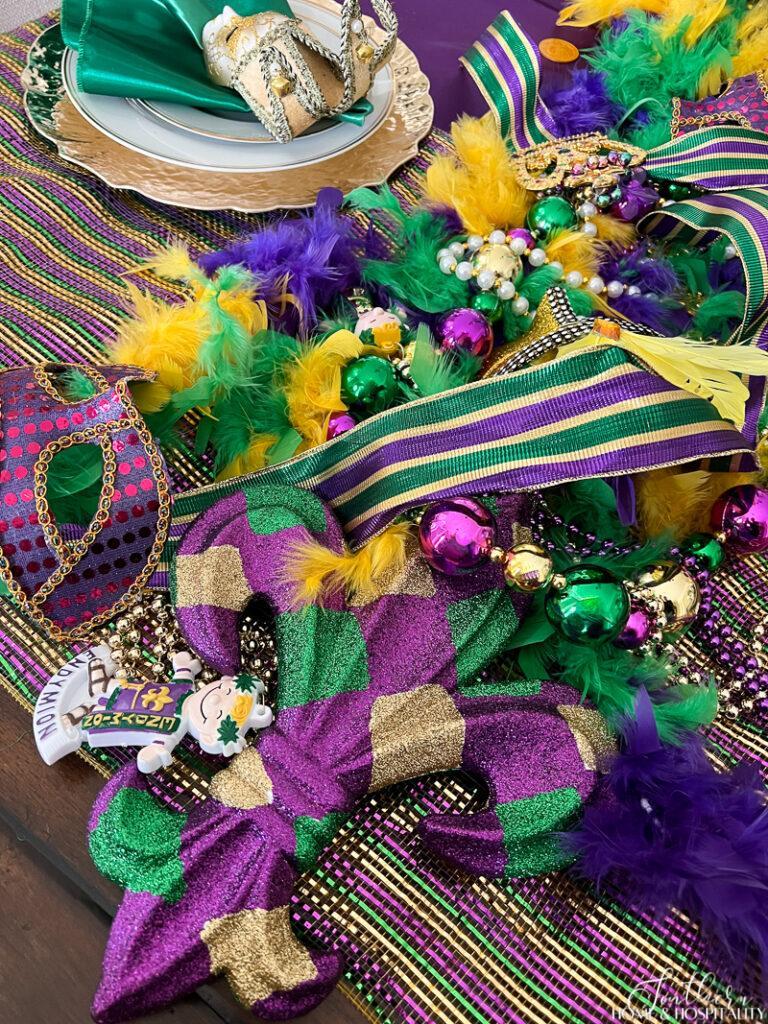 Mardi Gras table decor with feather boa, fleur de lis, beads, masks, and ribbon