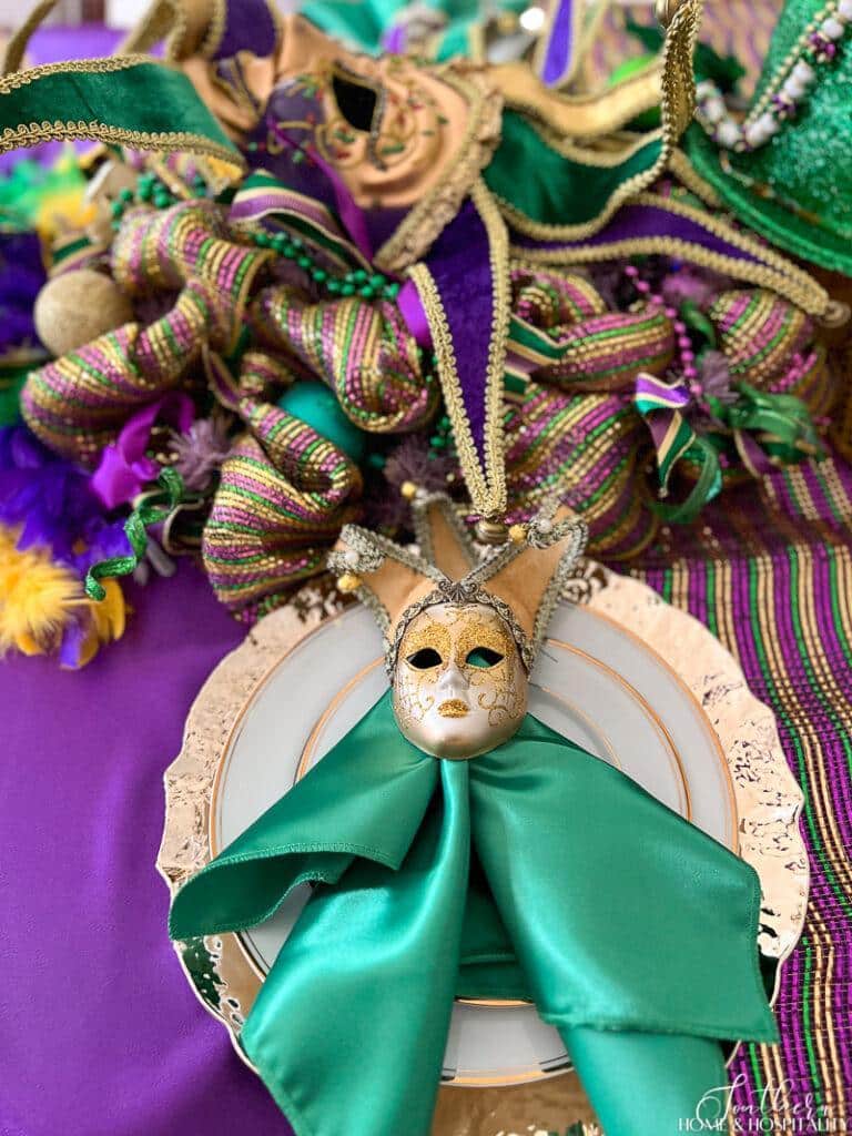 Green satin napkin, gold jester face, white and gold china, and gold charger on Mardi Gras table setting