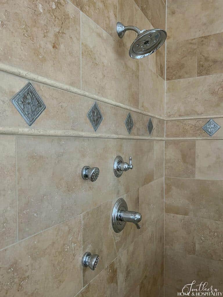 Travertine shower with polished chrome fixtures and metal accent tile
