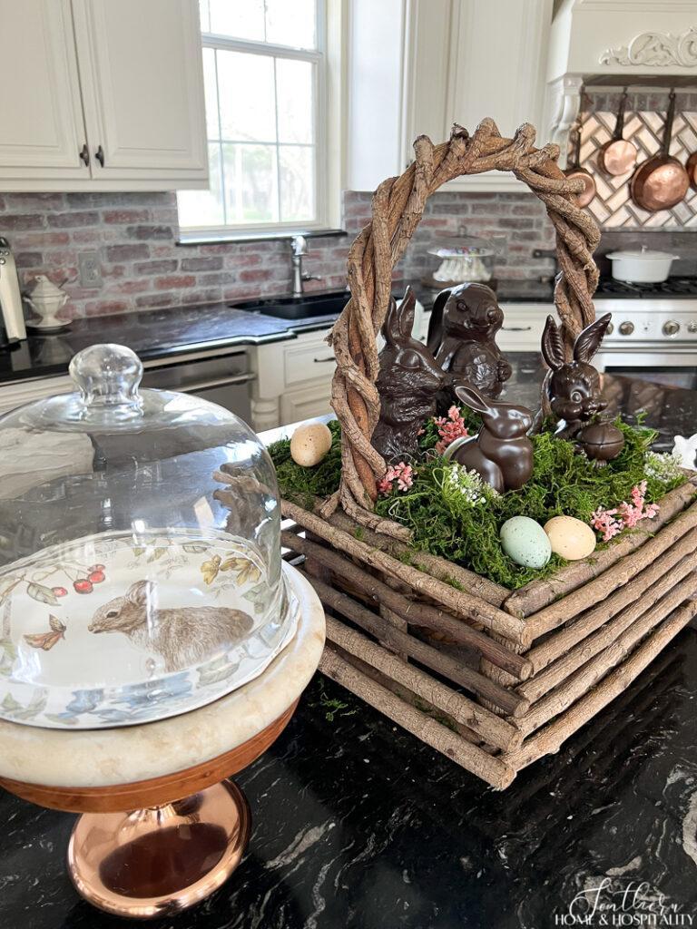 Easter kitchen decor with bunny plate under cloche pedestal and rustic basket with moss, eggs, and bunnies