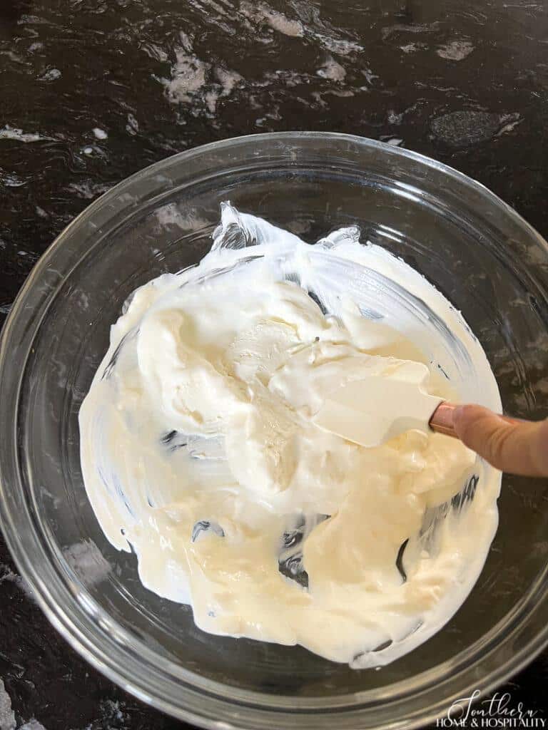 Mixing cream cheese, mayonnaise, and sour cream by hand in a bowl