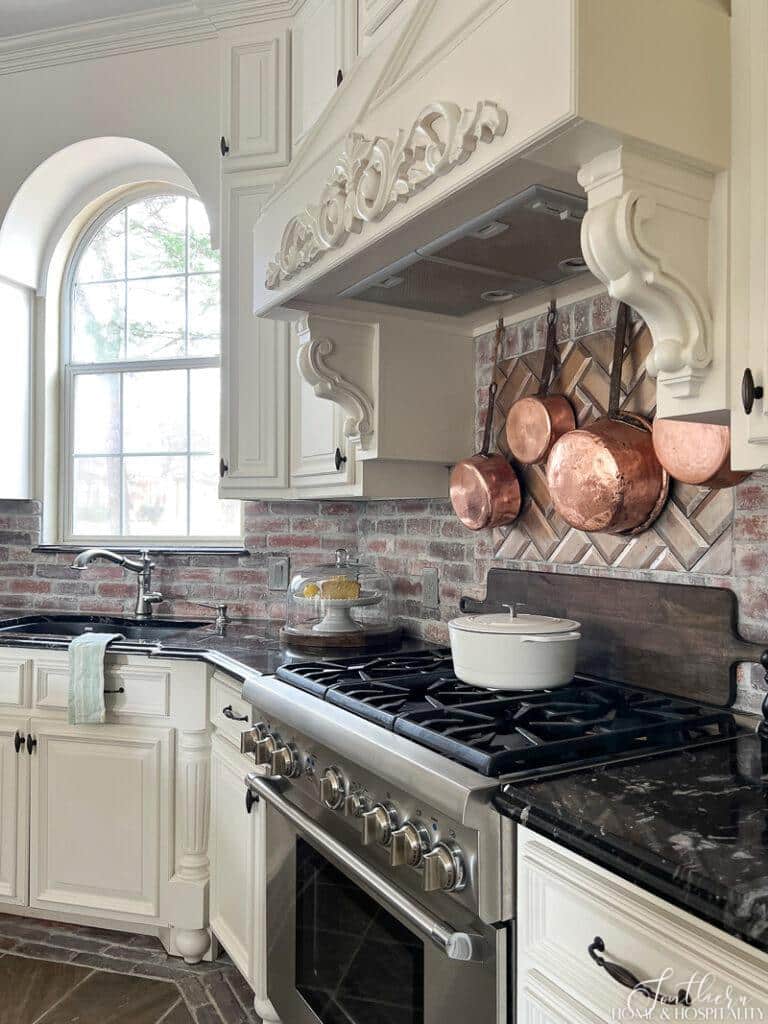 French country kitchen range and vent hood with copper pots and brick backsplash