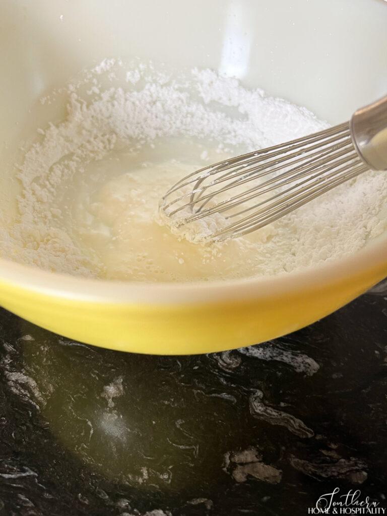 Whisking powdered sugar, lemon juice, and milk together to make lemon glaze