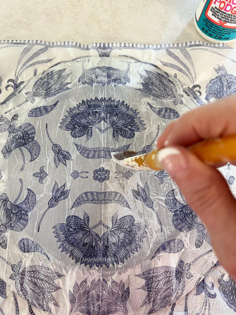 Painting mod podge over napkin on a plate