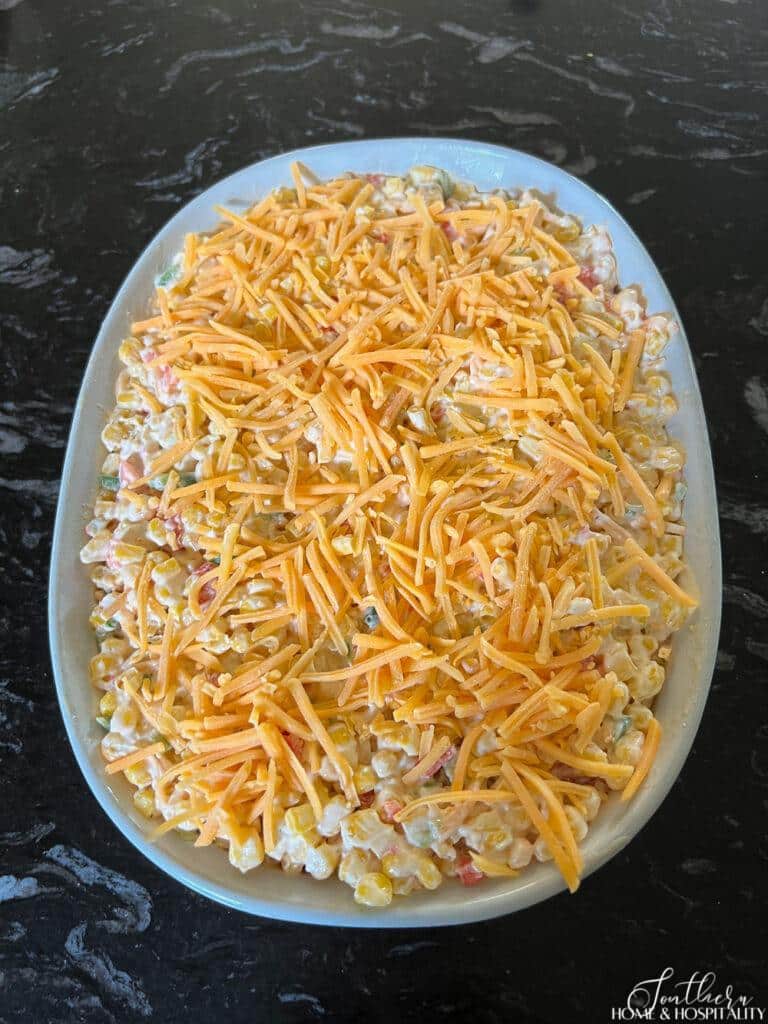 Unbaked jalepeno corn casserole mixture in baking dish topped with shredded cheese