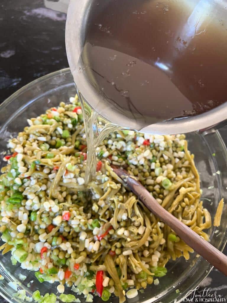 Pouring the oil and vinegar dressing over English pea, green bean, and corn salad