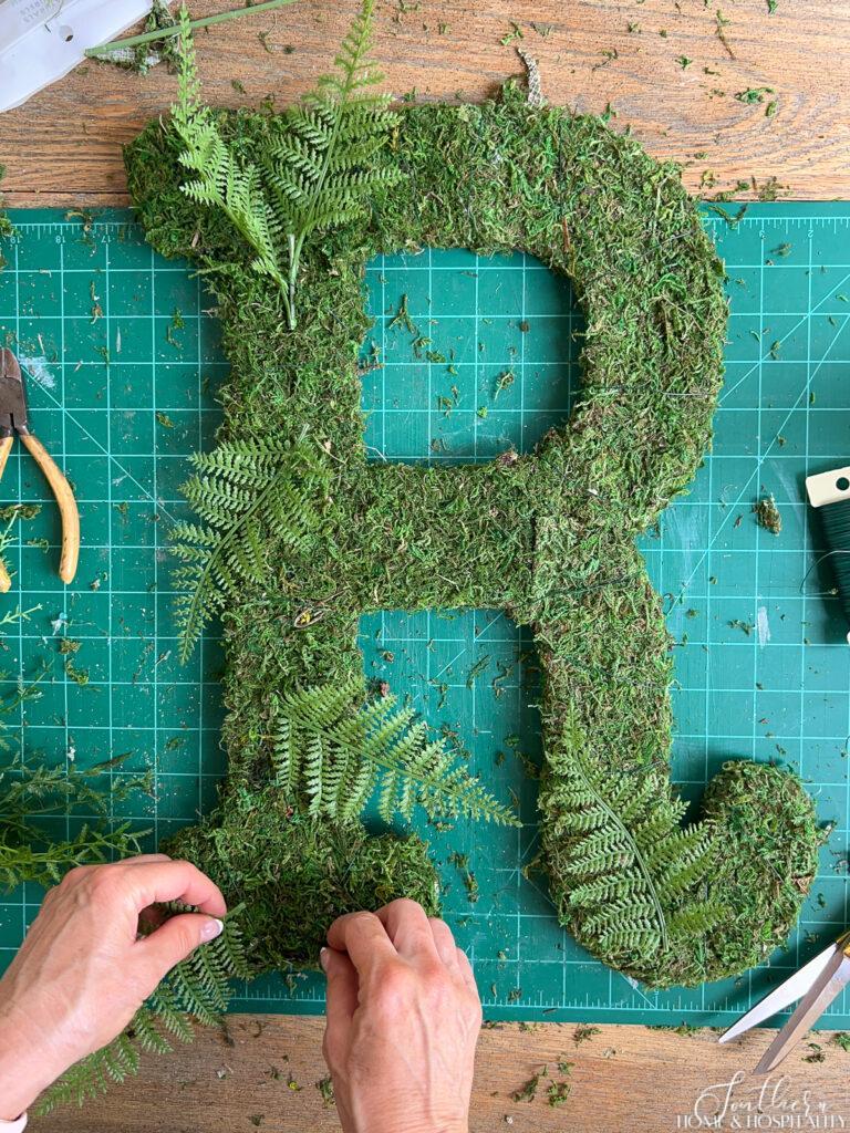 Adding faux florals to moss letter wreath